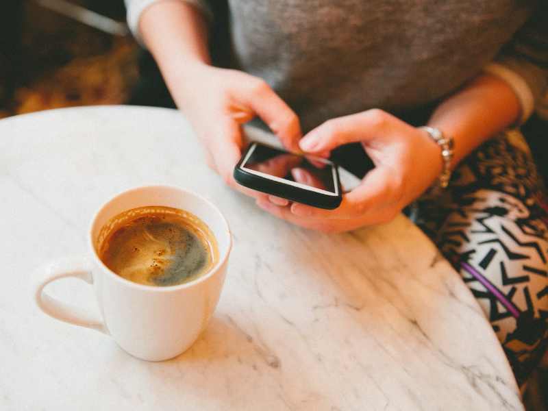 Woman texting, coffee on table